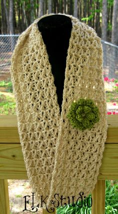 a crocheted scarf with a green flower on the front and side, hanging from a wooden fence