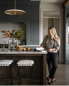 a woman is standing at the kitchen island reading a book and looking into the distance