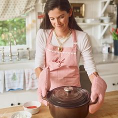 a woman in an apron is preparing food on the kitchen counter with a large pot