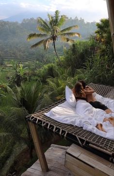 two people laying in a hammock on the side of a hill with palm trees