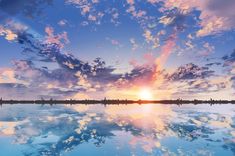 the sky is reflected in the water as the sun sets over the horizon with clouds