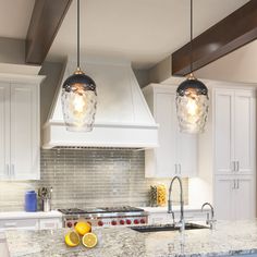 two lights hanging over a kitchen island with marble counter tops and white cabinets in the background