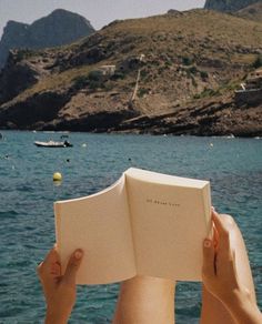 a person is reading a book by the water with boats in the ocean behind them