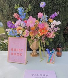 a vase filled with lots of flowers next to a guest book on top of a table