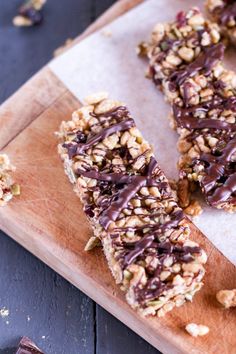 granola bars on a cutting board with chocolate drizzled over them and chopped nuts