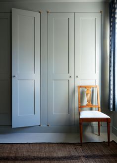 an empty chair sits in front of white closets with doors on each side and a window behind it