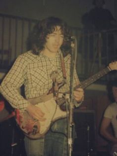 a man standing in front of a microphone while holding a guitar