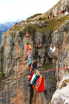 people hanging out on the edge of a cliff with flags strung from it's sides