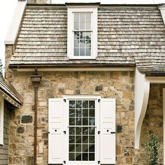 an old stone house with white shutters and a cat sitting on the front lawn