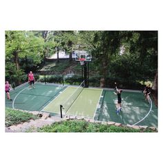 people playing tennis on an outdoor court in the park, surrounded by trees and bushes