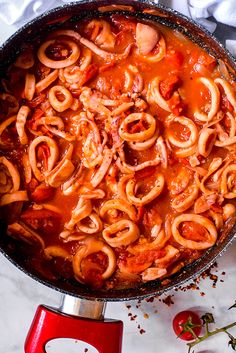 a pan filled with pasta and sauce on top of a counter next to tomatoes, pepperoni and garlic