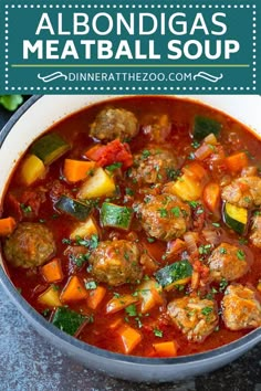 a bowl filled with meatball soup on top of a table next to a spoon