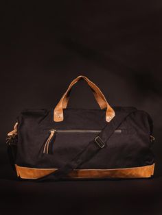 Black colored handcrafted canvas duffle bag with leather straps on black studio background. Black Rectangular Satchel With Canvas Lining, Black Canvas Tote Duffle Bag, Black Canvas Duffle Bag Tote, Black Canvas Satchel With Canvas Lining, Weekend Tote Duffle Bag With Luggage Sleeve, Black Canvas Duffle Bag, Weekender Bag With Leather Trim For Everyday Use, Waxed Canvas Tote For Weekend Trips, Rectangular Weekender Bag With Leather Trim For Everyday Use