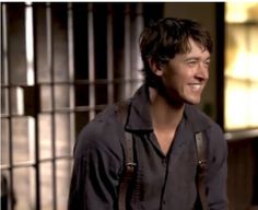 a man with suspenders smiling in front of a jail cell