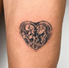 a heart shaped tattoo with two people in it's center, on the side of a woman's thigh