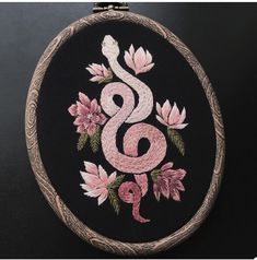 an embroidered snake on a black background with pink flowers in the center and green leaves around it