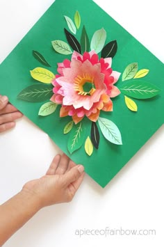 someone is making a paper flower on a green piece of paper that has leaves and flowers cut out of it