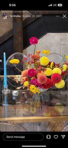 a vase filled with colorful flowers sitting on top of a glass table next to a blue candle