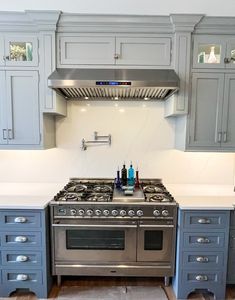 a stove top oven sitting inside of a kitchen next to gray cupboards and drawers