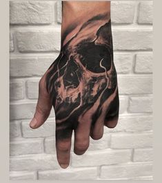 a man's hand with a black and grey tattoo on it, which has a skull in the middle