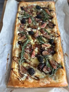 a long rectangular pizza with olives, blackberries and other toppings on it