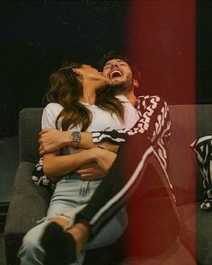 a man and woman sitting on a couch with their arms around each other as they kiss