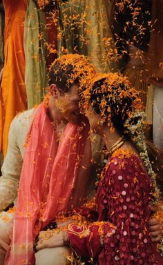 a man and woman sitting next to each other in front of orange petals on the ground