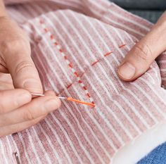 someone is stitching something on a piece of fabric with needles and thread in their hands