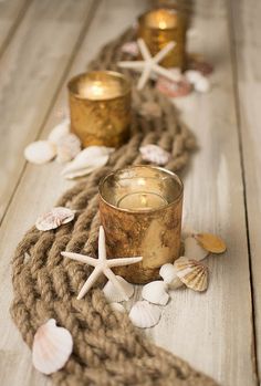 two candles are sitting on a rope with seashells and starfish around it