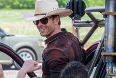 a man wearing a cowboy hat and sunglasses driving a tractor with people in the background