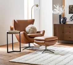 a chair and ottoman in a room with wood flooring, white rug and large windows