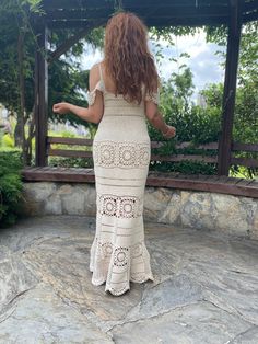 a woman in a crochet dress is standing on a stone patio and looking at the gazebo