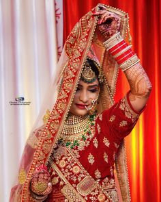 a woman in a red and gold bridal outfit is holding her hands up to her head