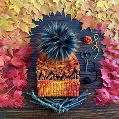 a knitted hat sits on top of some twigs and leaves with scissors in the background