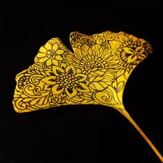 a yellow leaf with intricate designs on it's side, against a black background