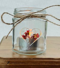 a glass jar filled with flowers and a heart cut out in the middle on top of a wooden table