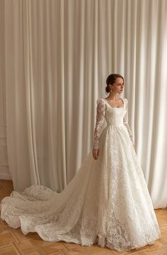 a woman in a white wedding dress standing on a wooden floor next to a curtain