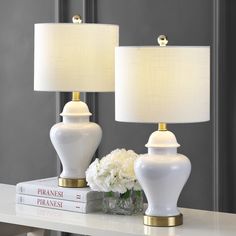 two white lamps sitting on top of a table next to a vase with flowers in it