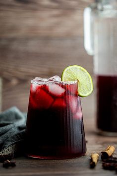 a pitcher filled with liquid and a lime slice next to it on a wooden table