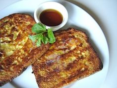 two pieces of french toast on a white plate with a cup of tea and sauce