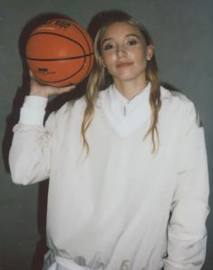 a woman holding a basketball in her right hand and posing for the camera with both hands