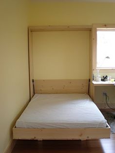 a small bed in the corner of a room next to a window with no curtains