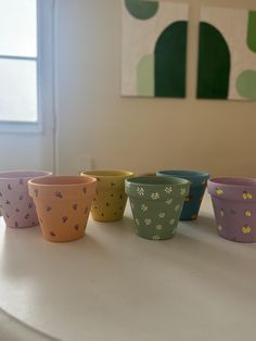 five small cups sitting on top of a white table next to a window in a room