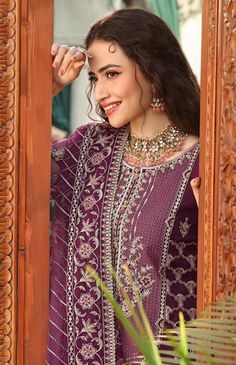 a woman in a purple dress standing next to a wooden frame and looking into the mirror