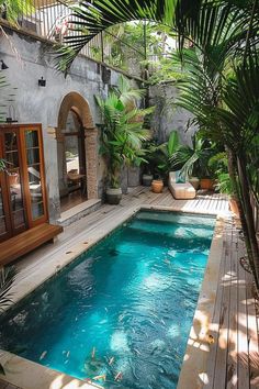 an outdoor swimming pool surrounded by greenery and wooden decking, next to a patio