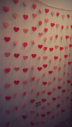 red paper hearts hanging from the wall in front of a white curtain with pink trim