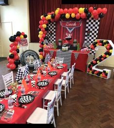 a table set up with black and white checkered tables cloths, red runneres, orange and yellow balloons