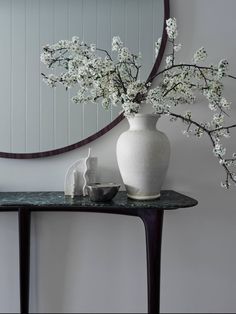 a white vase sitting on top of a table next to a mirror with flowers in it