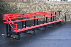 a red bench sitting in front of a stone wall next to a black metal fence