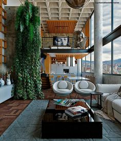 a living room filled with furniture next to a tall window covered in greenery on top of a hard wood floor